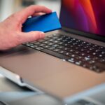 Close-up of a hand holding an external hard drive over a laptop keyboard.