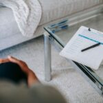 From above of blurred unrecognizable female psychologist sitting in office near table with clipboard and pen during session in office